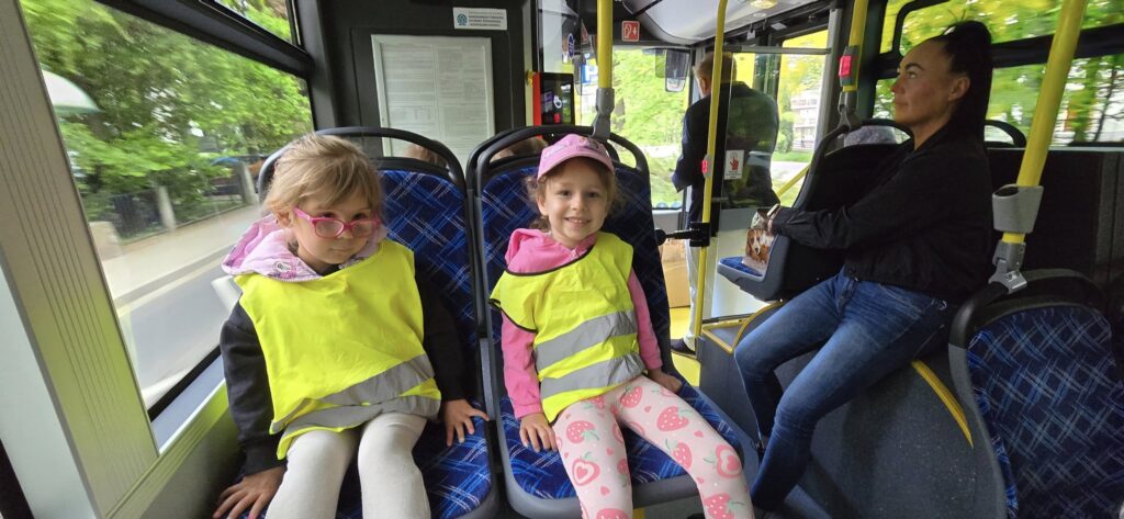 Dwie dziewczynki w kamizelkach odblaskowych siedzą w autobusie wodorowym MZUK.